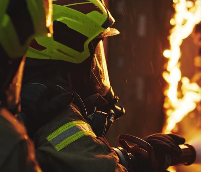 dramatic shot of firemen holding hose spraying water on to burning hot flames